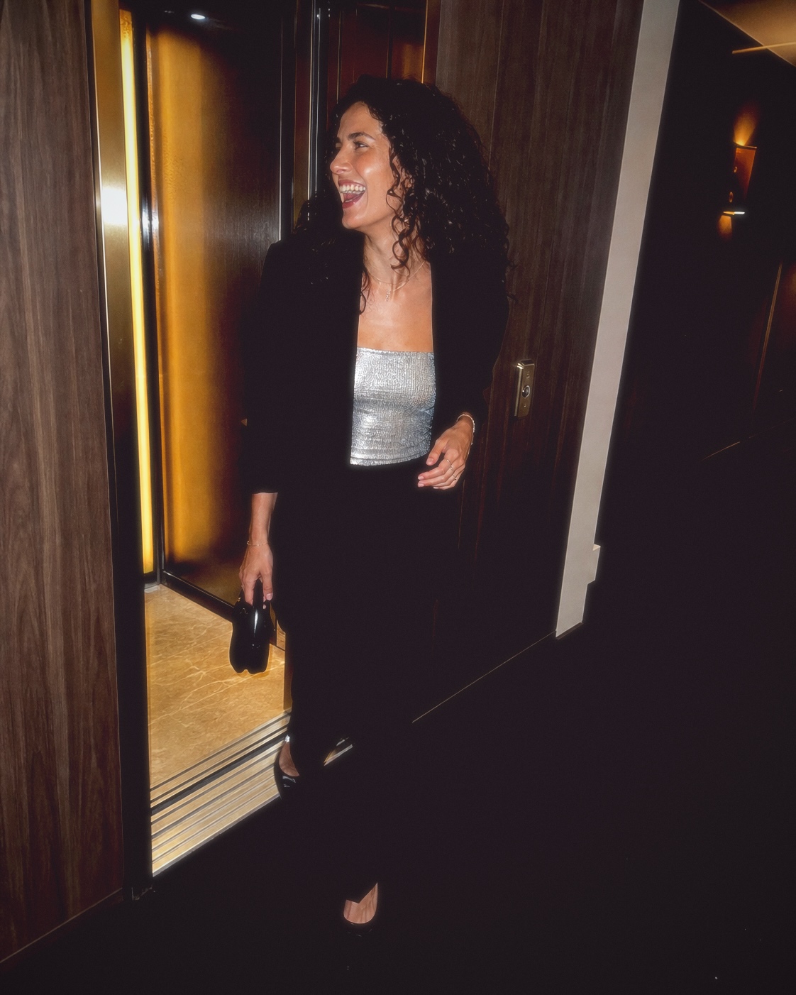 An adult woman laughing as she steps from a hotel lift, finished with Fold I.